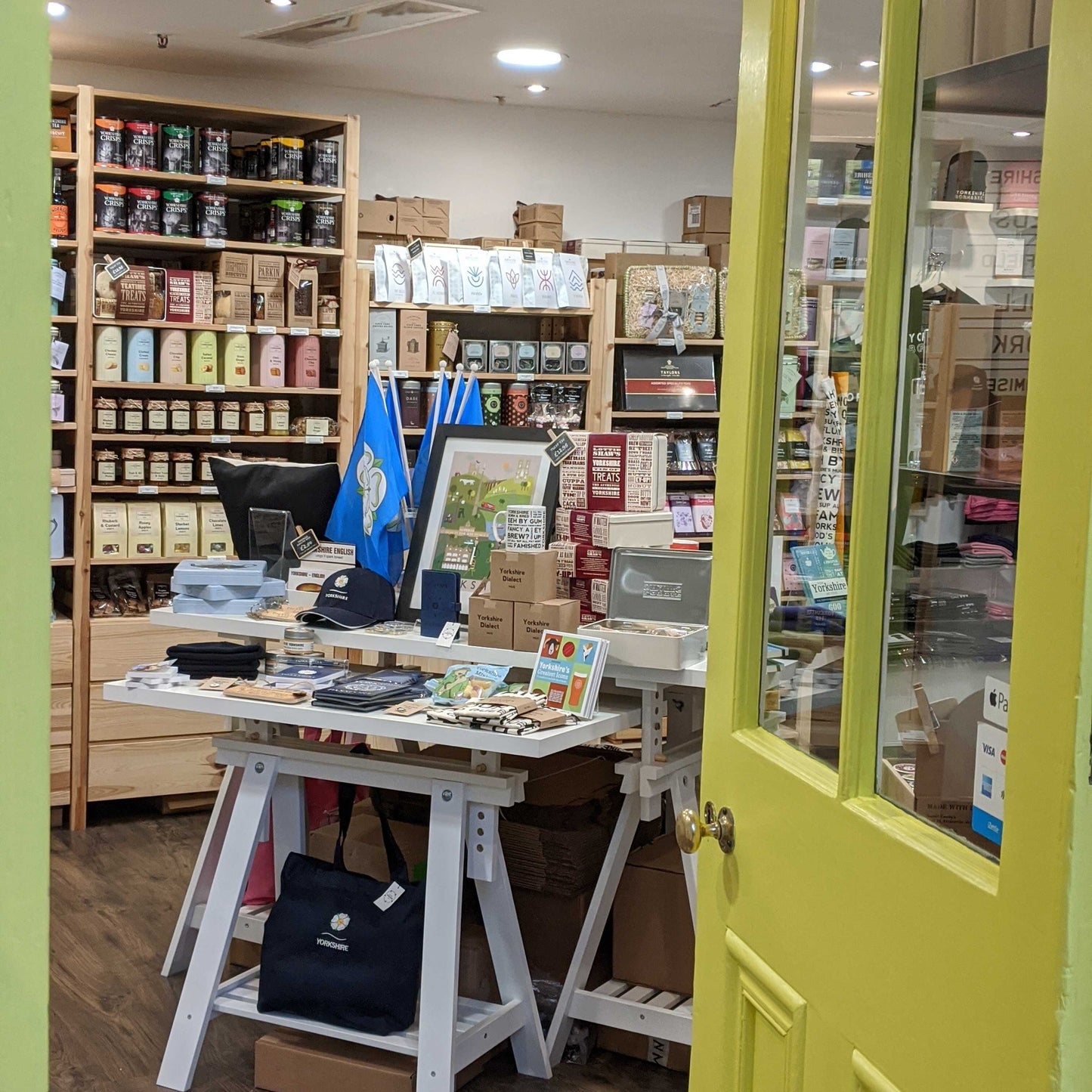 Photograph of the Great Yorkshire Shop taken from the entrance of the store, showing the main table with a collection of Yorkshire souvenirs and the back shelves holding different foods