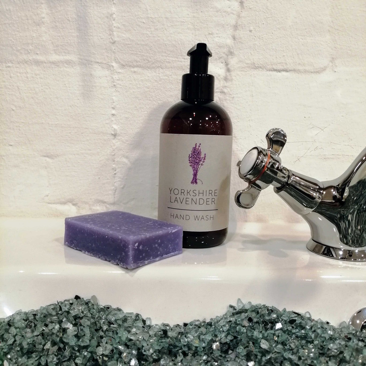 Photograph of a purple bar of soap and a dark brown bottle of lavender hand soap set on the side of a sink. 